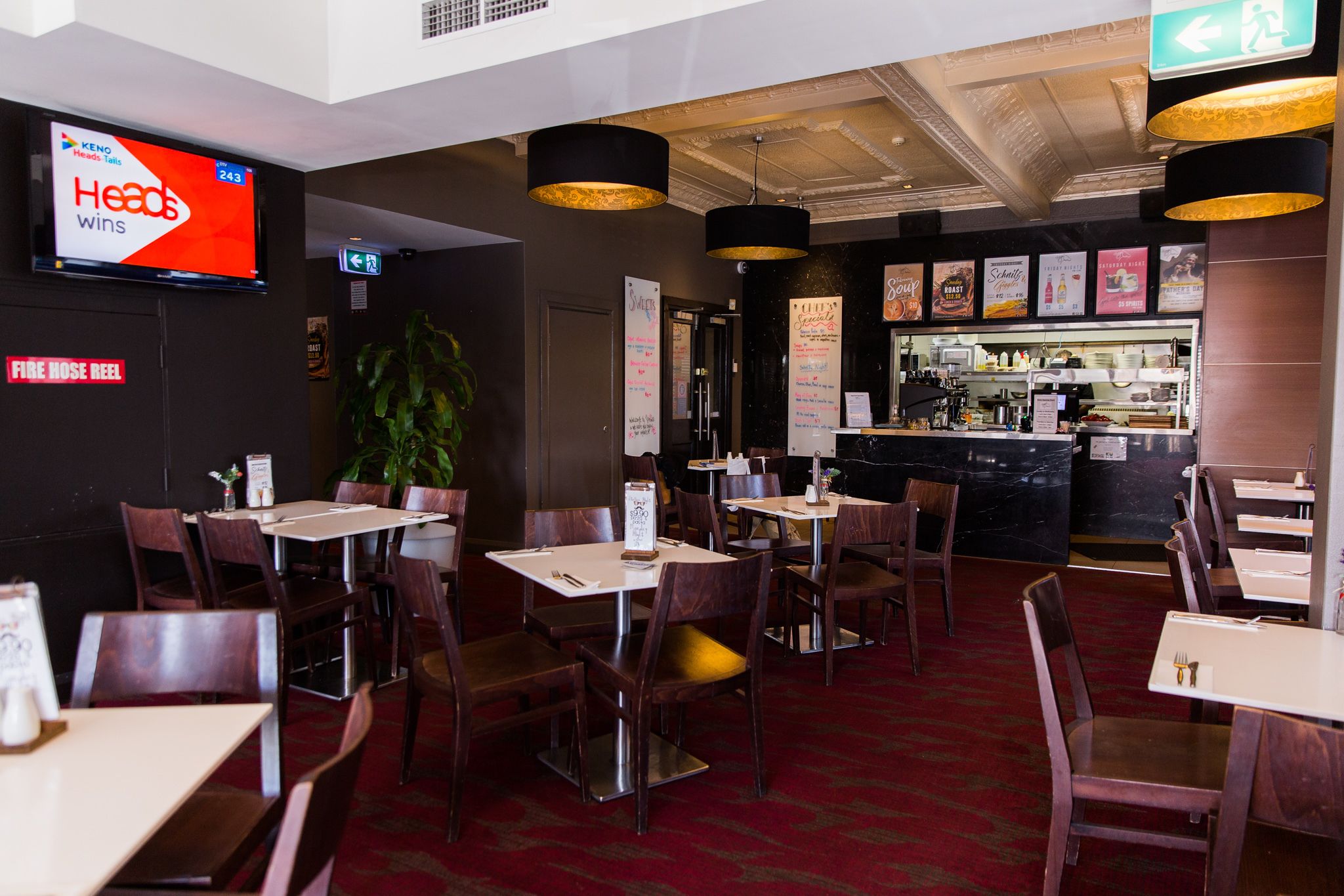 Um restaurante com mesas, cadeiras, um espaço de bar e uma televisão exibindo 'Heads Wins'.