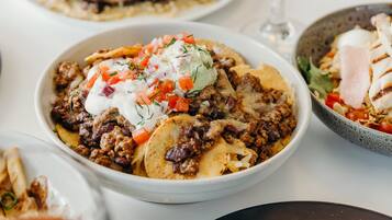 A table with various dishes, including a bowl of chili, a plate of nachos, and a glass of white wine.