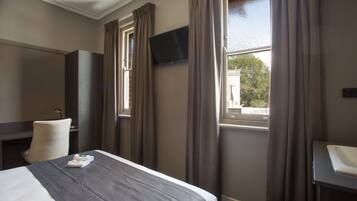 A hotel room with a bed, a desk, a chair, a TV, and a window with curtains.