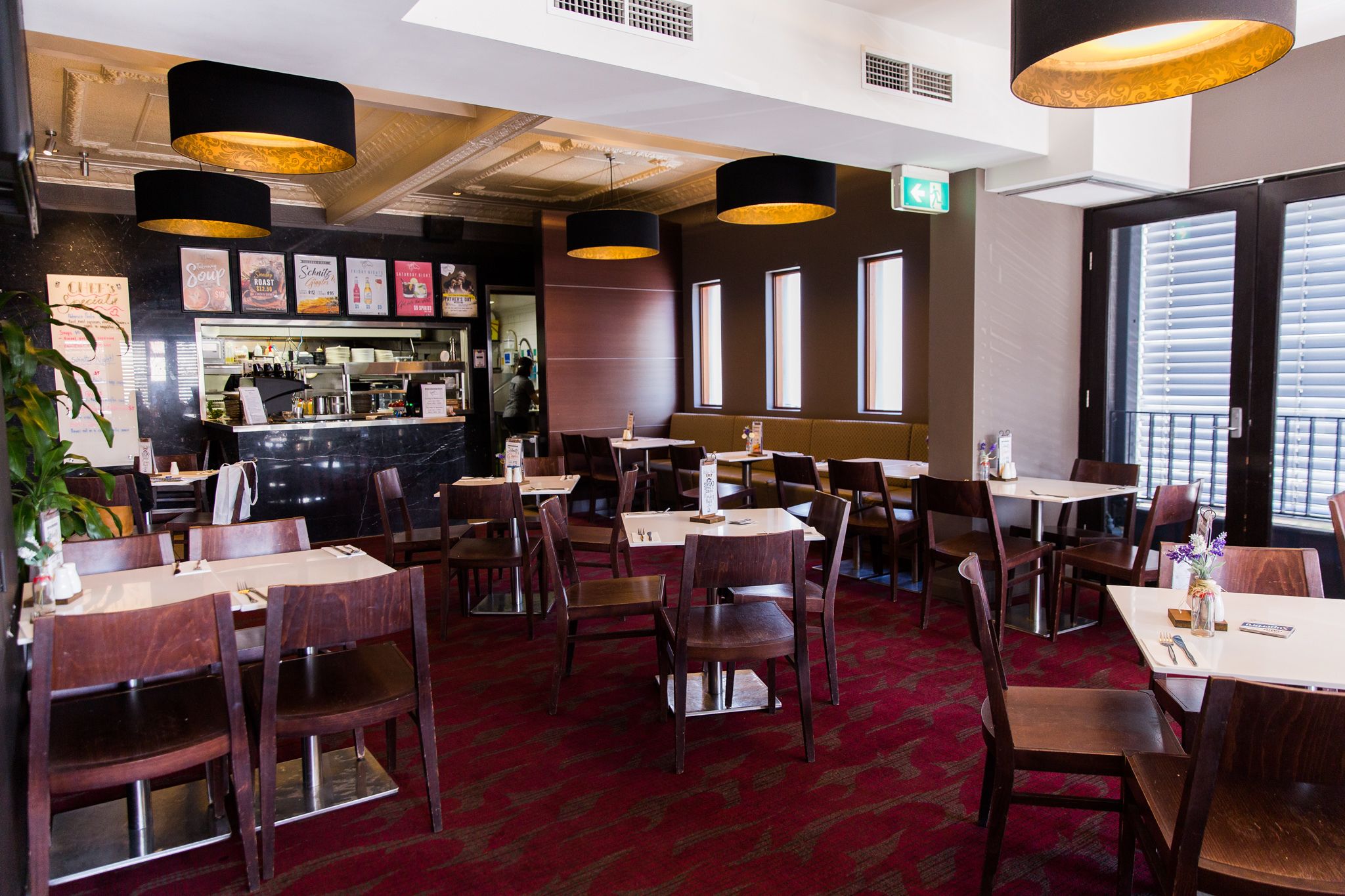 A restaurant with multiple tables and chairs, a bar area, and large windows allowing natural light.