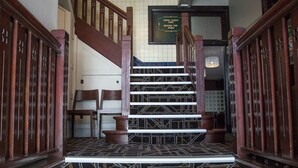 A grand staircase with intricate black and gold patterns, wooden railings, and a chandelier. - Nags Head Hotel (Adamstown)