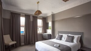A hotel room with a large bed, a bedside table, a chair, and a window with curtains. - Nags Head Hotel (Adamstown)