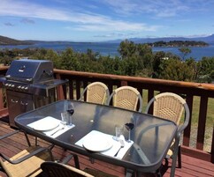 Una terraza con mesa para dos, una parrilla y vistas a un lago y montañas.