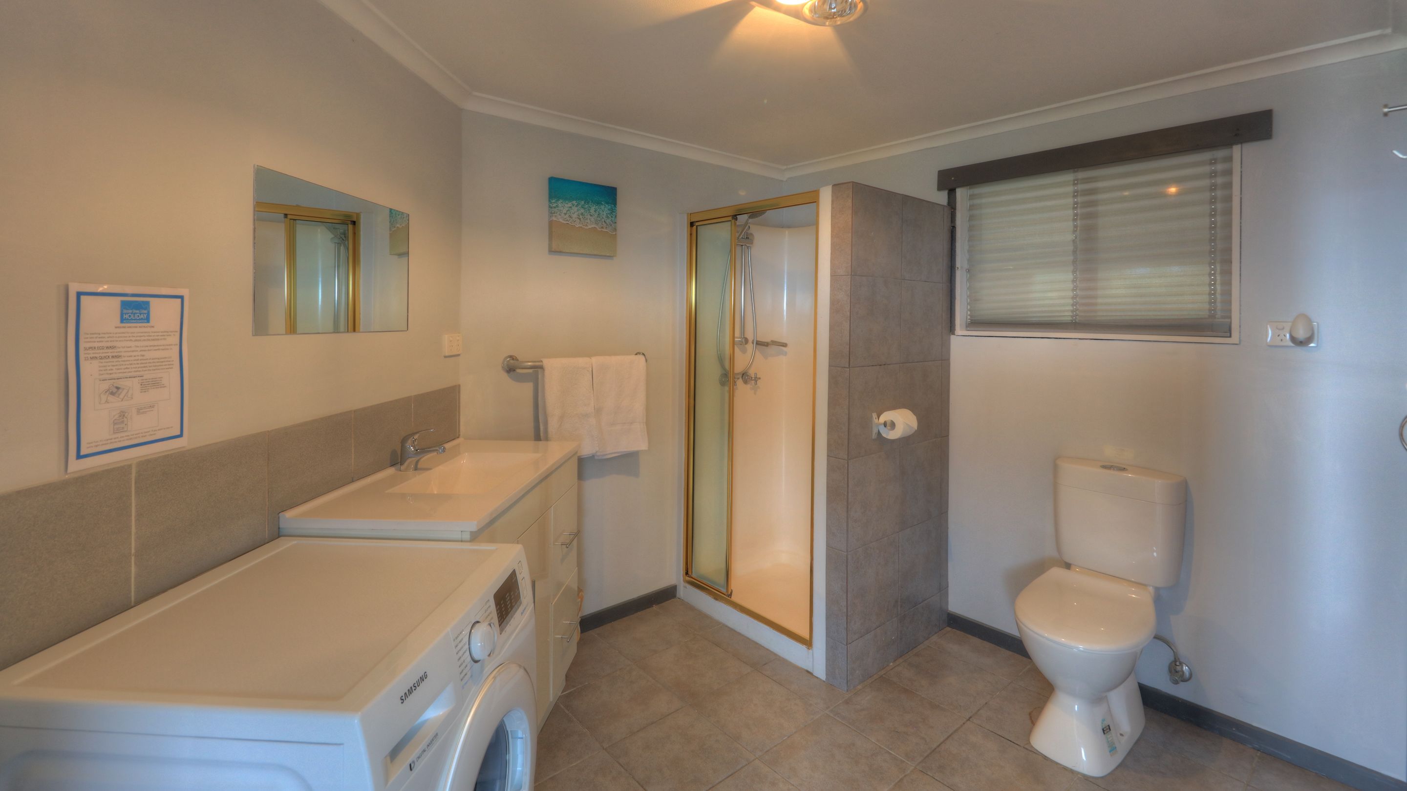 A bathroom with a washing machine, a glass-enclosed shower, and a toilet.