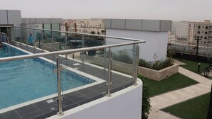 Una piscina en la azotea con barandilla de cristal, rodeada de jardines y vistas a la ciudad.