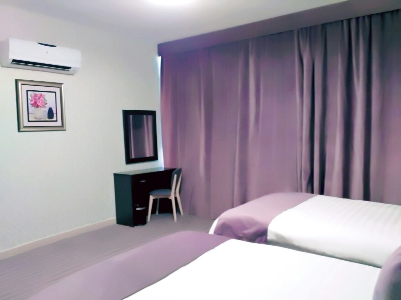 Habitación de hotel con dos camas, un escritorio, una silla, aire acondicionado y un cuadro en la pared.