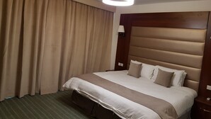 Habitación de hotel con una cama grande, cortinas color beige y una lámpara de techo moderna.