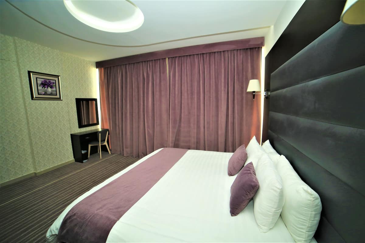 A hotel room with a large bed, a desk, a chair, and a window with curtains.