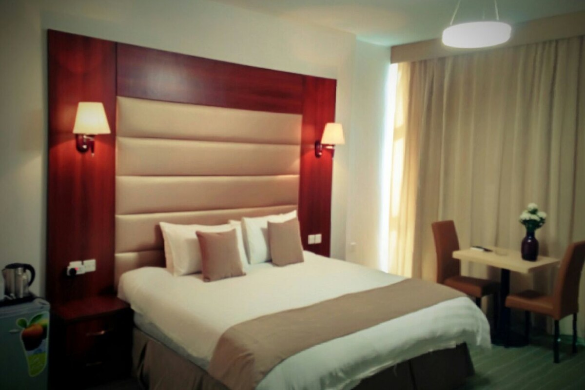 A hotel room with a large bed, two bedside tables, a desk, and a chair.
