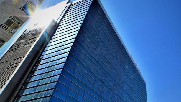 Un edificio moderno de cristal con fachada reflectante, ventanas amplias y una entrada destacada.