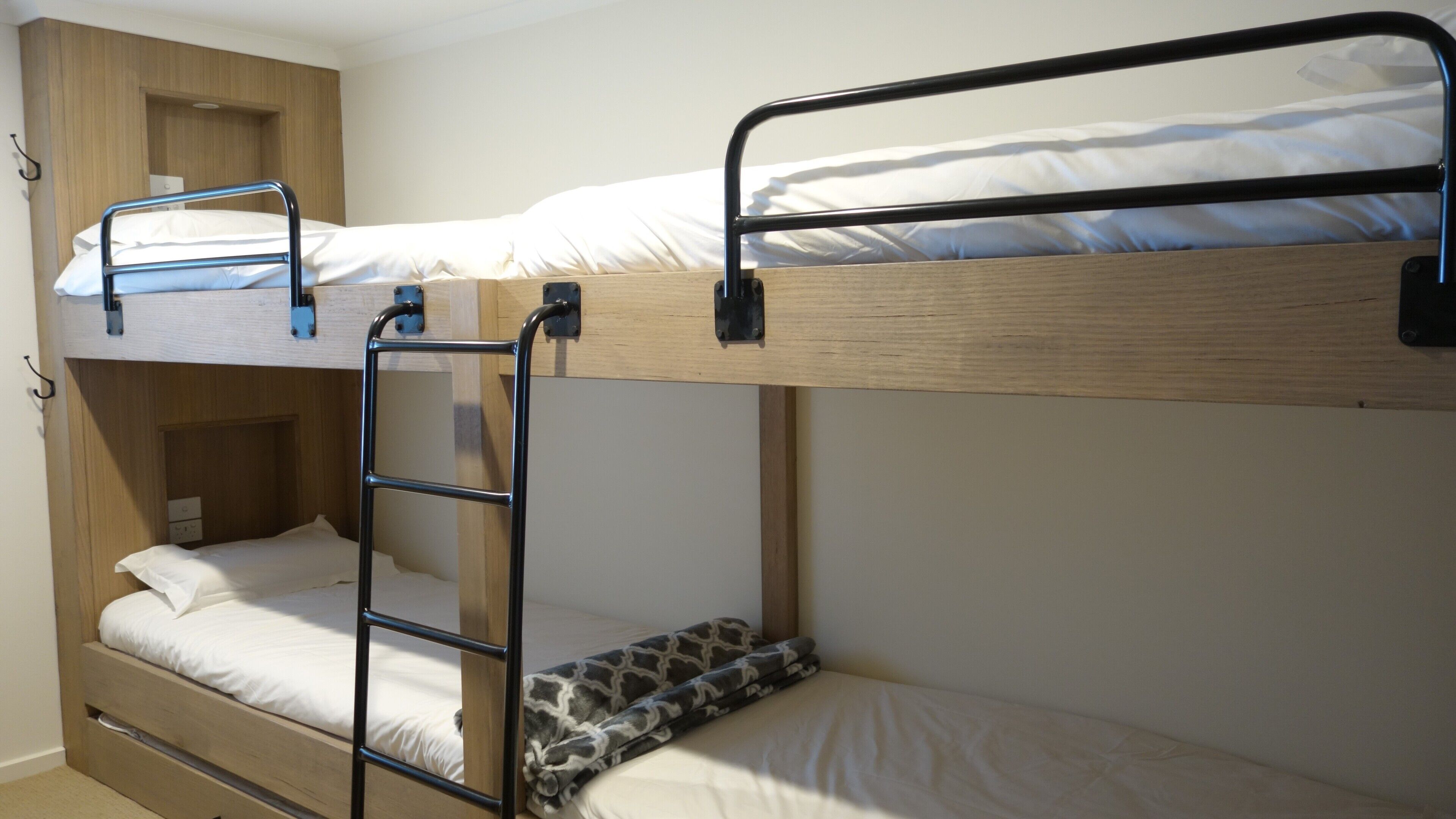 A bunk bed room with a ladder, a wooden wardrobe, and a small desk.