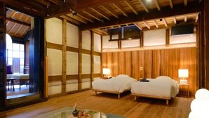 Une pièce de style japonais traditionnel, avec un sol recouvert de tatamis, deux lits, une table basse en verre et une vue sur une autre pièce de style japonais, accessible par une porte coulissante.
