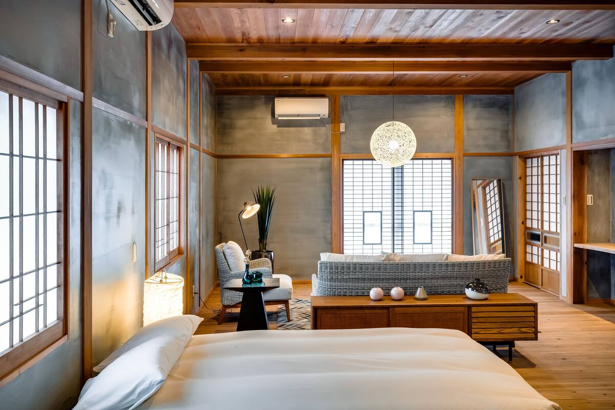 Ein traditionelles japanisches Schlafzimmer mit einem großen Bett, einer Sitzecke mit Kissen und Blick durch einen Shoji-Bildschirm.