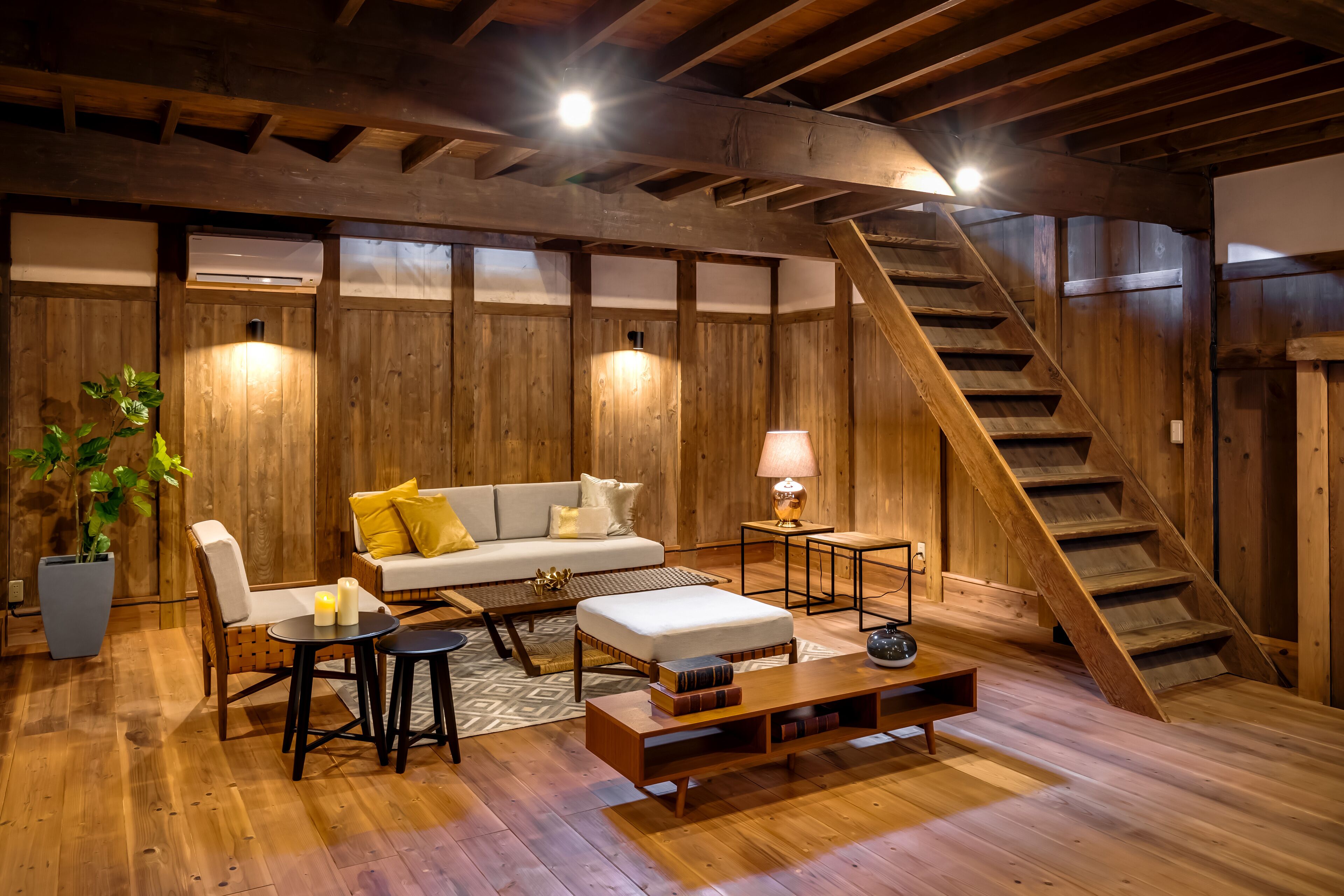 A cozy wooden-floored living room with a sofa, coffee table, and a staircase.