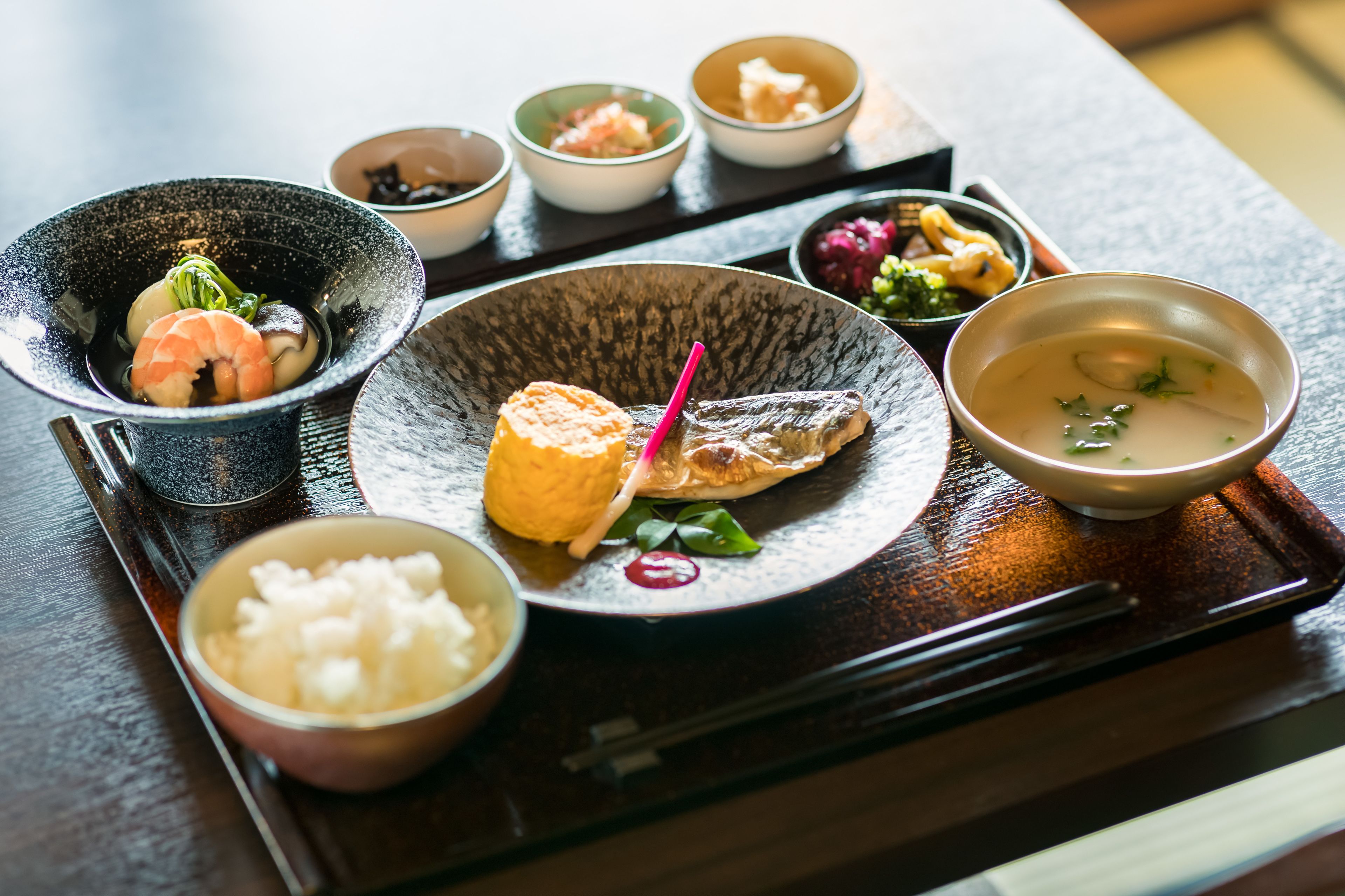 Una variedad de platos sobre una bandeja de madera, incluyendo un tazón de sopa, un plato con pescado y varios recipientes pequeños con diferentes comidas.