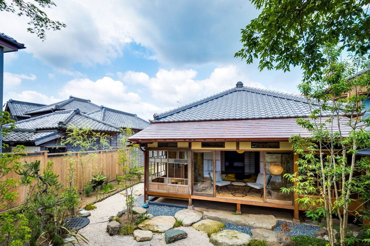Ein traditionelles japanisches Haus mit Holzwand, einem Ziegeldach und einem Garten mit Steinen und Pflanzen.