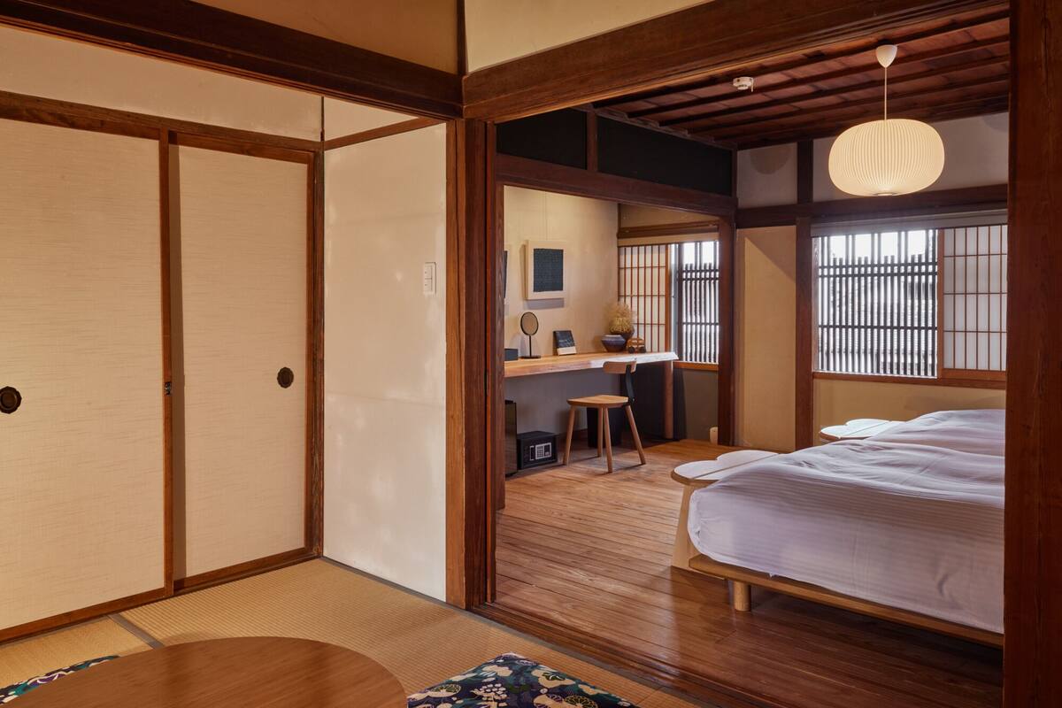 Ein traditioneller japanischer Raum mit Tatami-Boden, einem niedrigen Holztisch, einem Bett und einer Schiebetür.