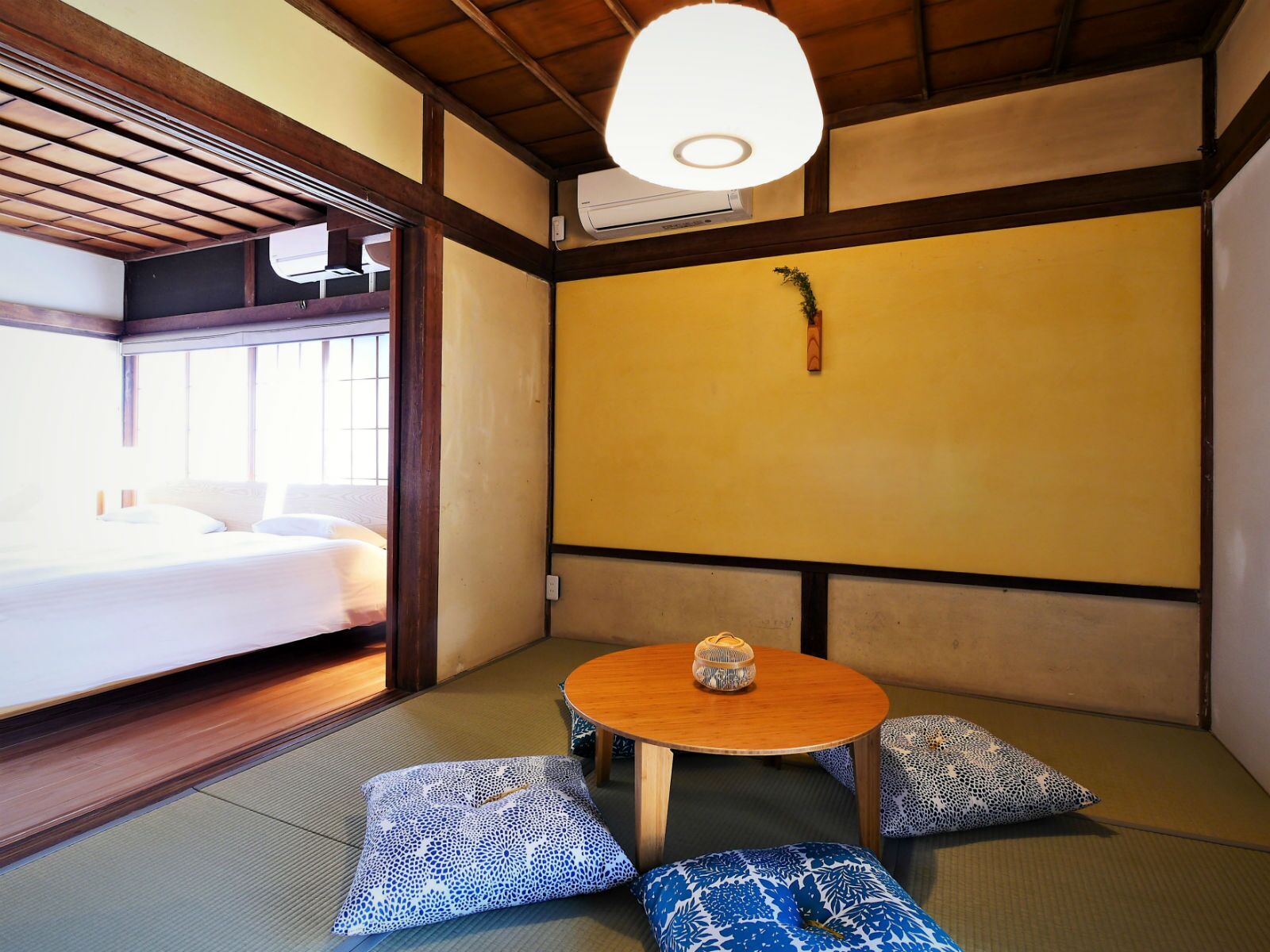 Una habitación tradicional japonesa con suelo de tatami, una mesa de madera baja y un cuenco decorativo, y una cama con ropa de cama blanca.