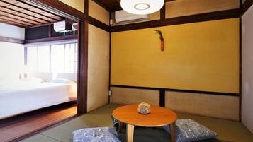 Una habitación tradicional japonesa con suelo de tatami, una mesa de madera baja y un cuenco decorativo, y una cama con ropa de cama blanca.