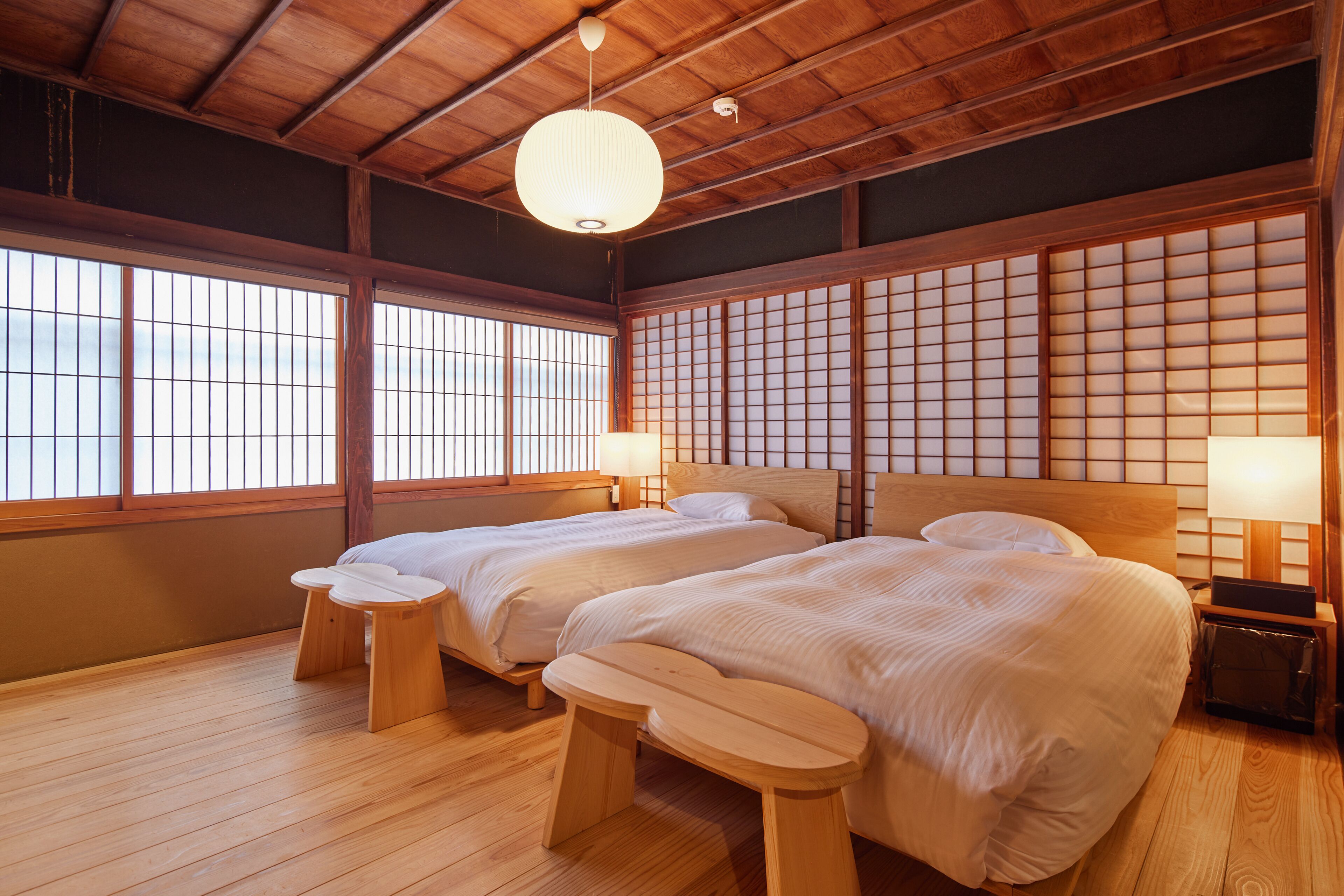 Una habitación tradicional japonesa con dos camas, suelo de madera, esteras de tatami, puertas correderas shoji e una lámpara colgante.