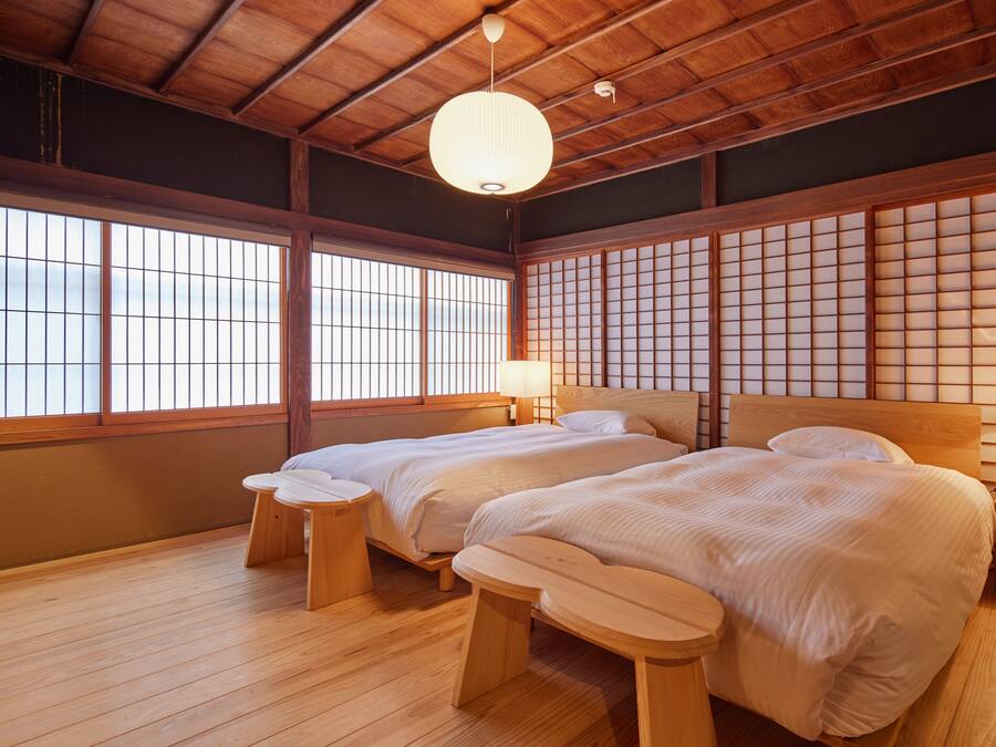 Una habitación tradicional japonesa con dos camas, suelo de madera, esteras de tatami, puertas correderas shoji e una lámpara colgante.
