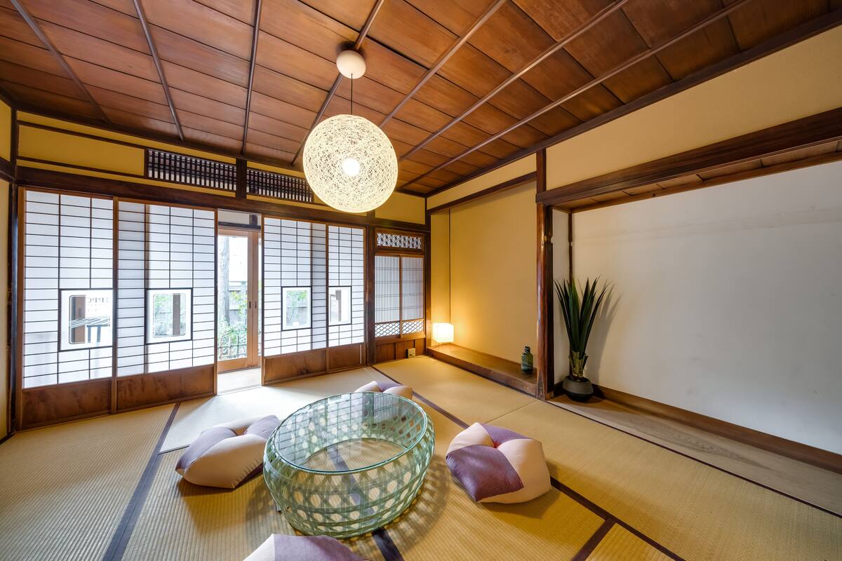 Ein traditioneller japanischer Raum mit Tatami-Boden, einem Glastisch, Kissen, Schiebetüren und einer Hängeleuchte.