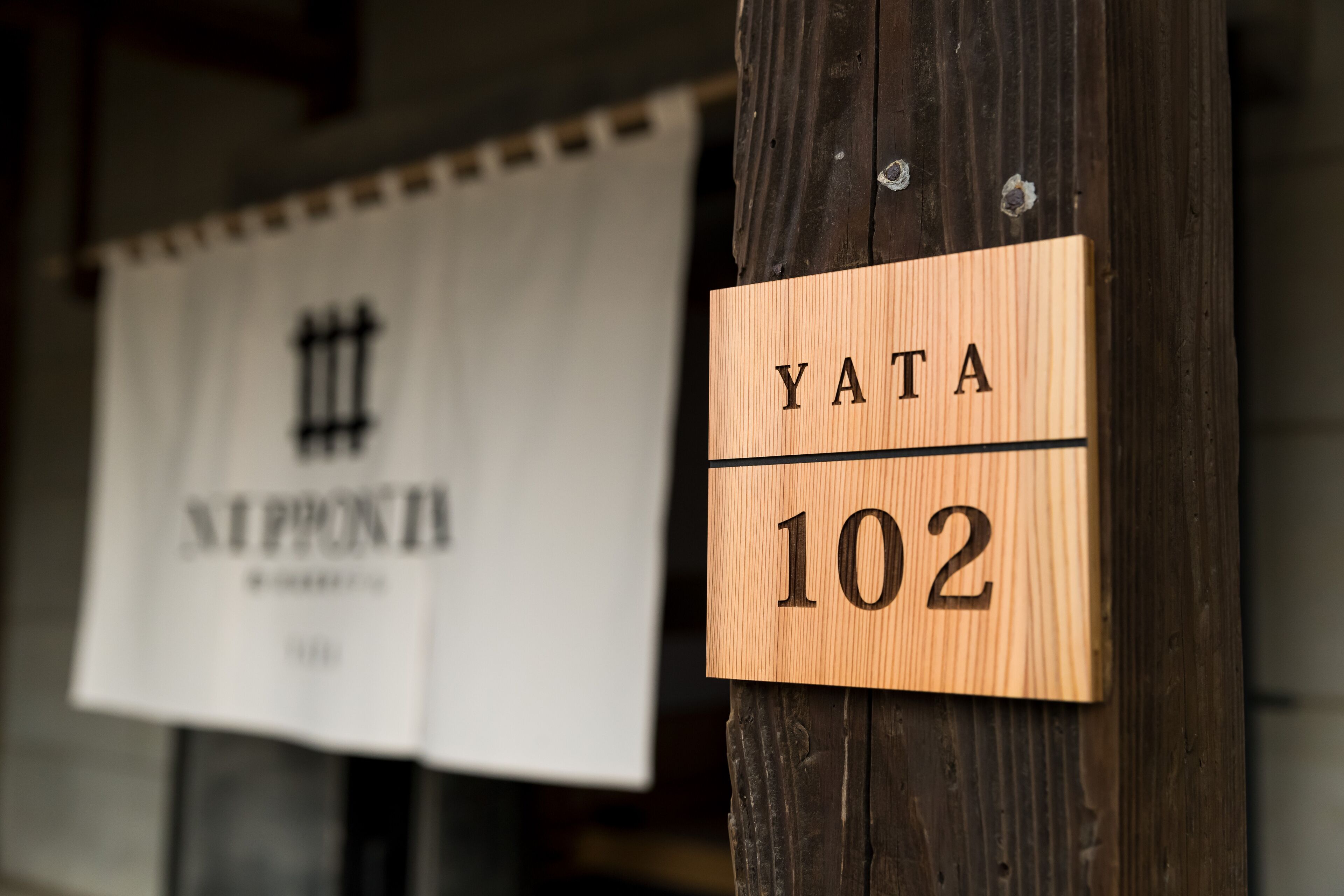 A wooden sign with the name 'YATA' and the number '102' on a wooden post.