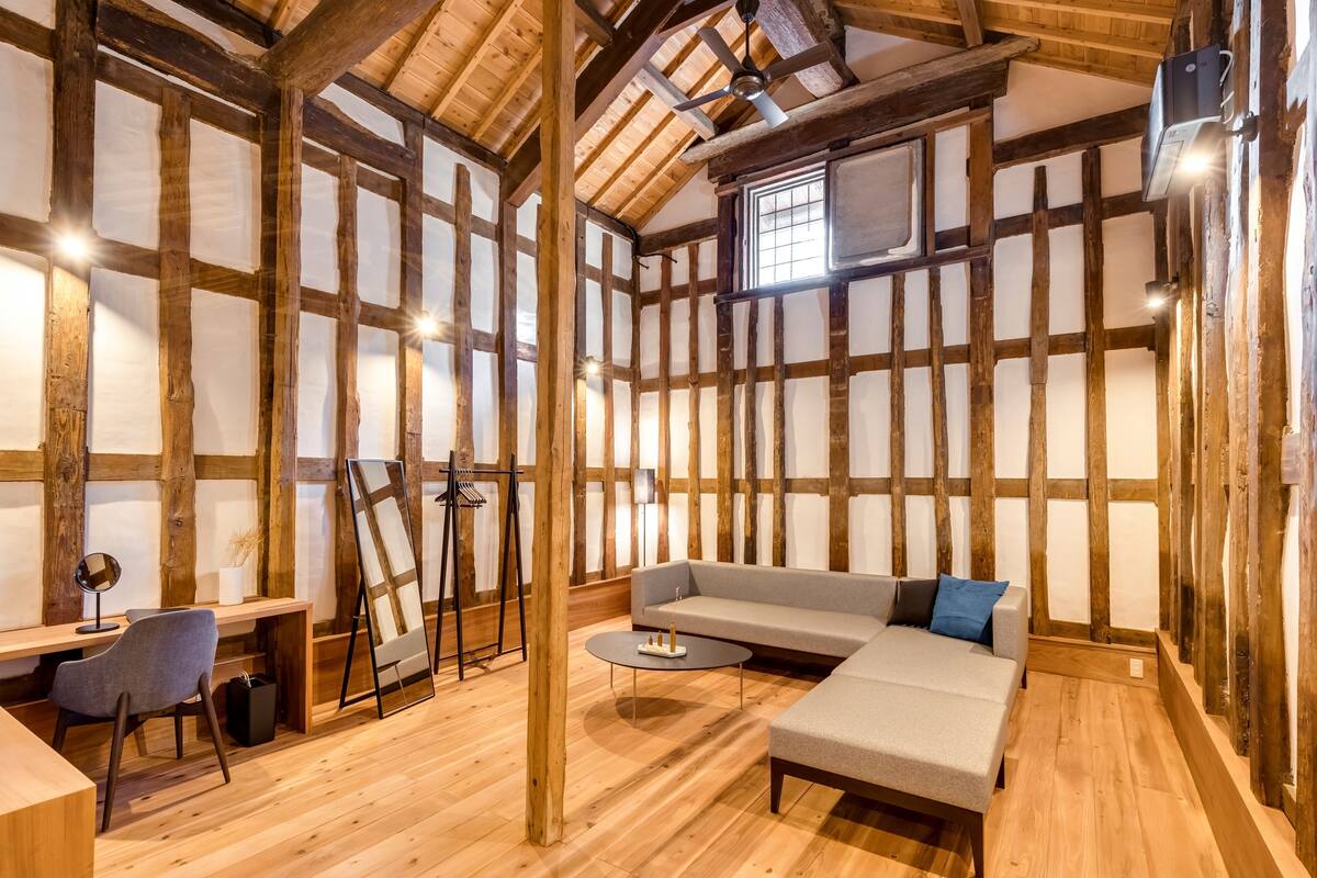Ein Zimmer mit freiliegenden Holzbalken, einem Sofa, einem kleinen Tisch und einem Schreibtisch mit Stuhl.