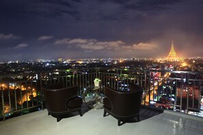 A balcony with two chairs and a small table, overlooking a cityscape with a prominent tower. - Pyay Garden Residence (Yangon)