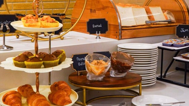 A buffet with various food items including bread, jam, muffins, and croissants. - Bizz The Hotel (Rajkot)