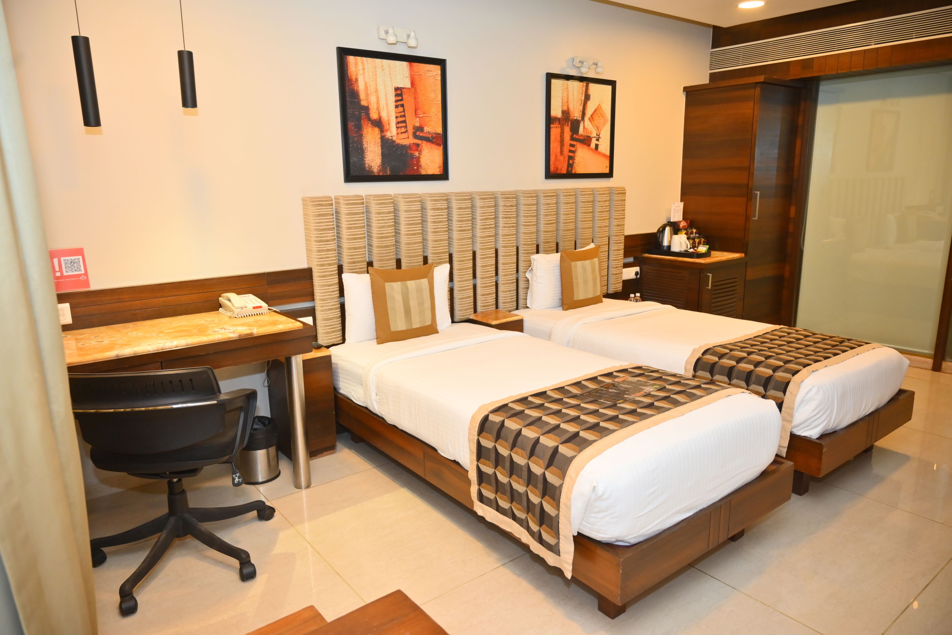 Een hotelkamer met twee bedden, een bureau met stoel, een kleine tafel en een prullenbak.