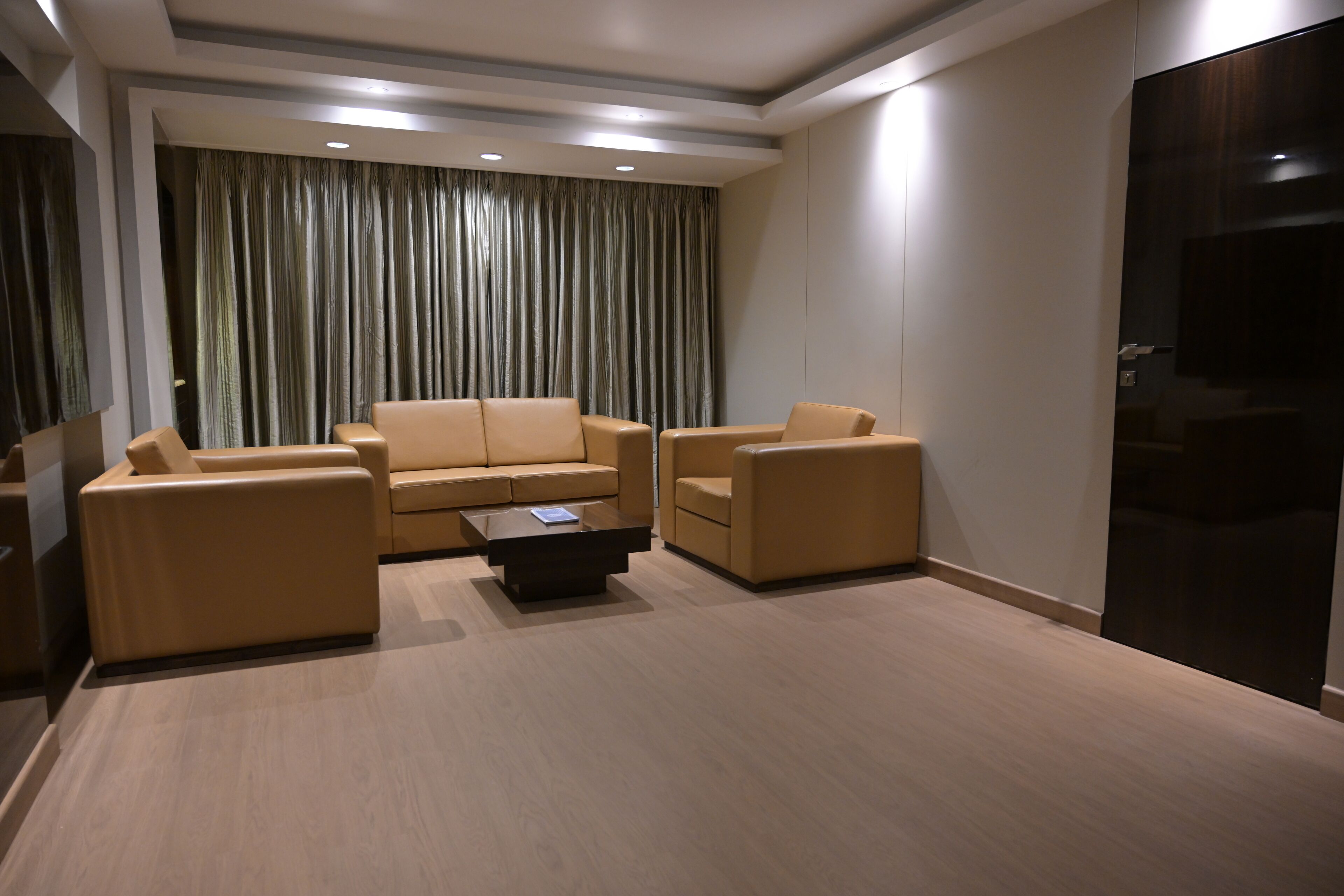 A modern living room with a beige sofa set, a coffee table, and a large window with curtains.