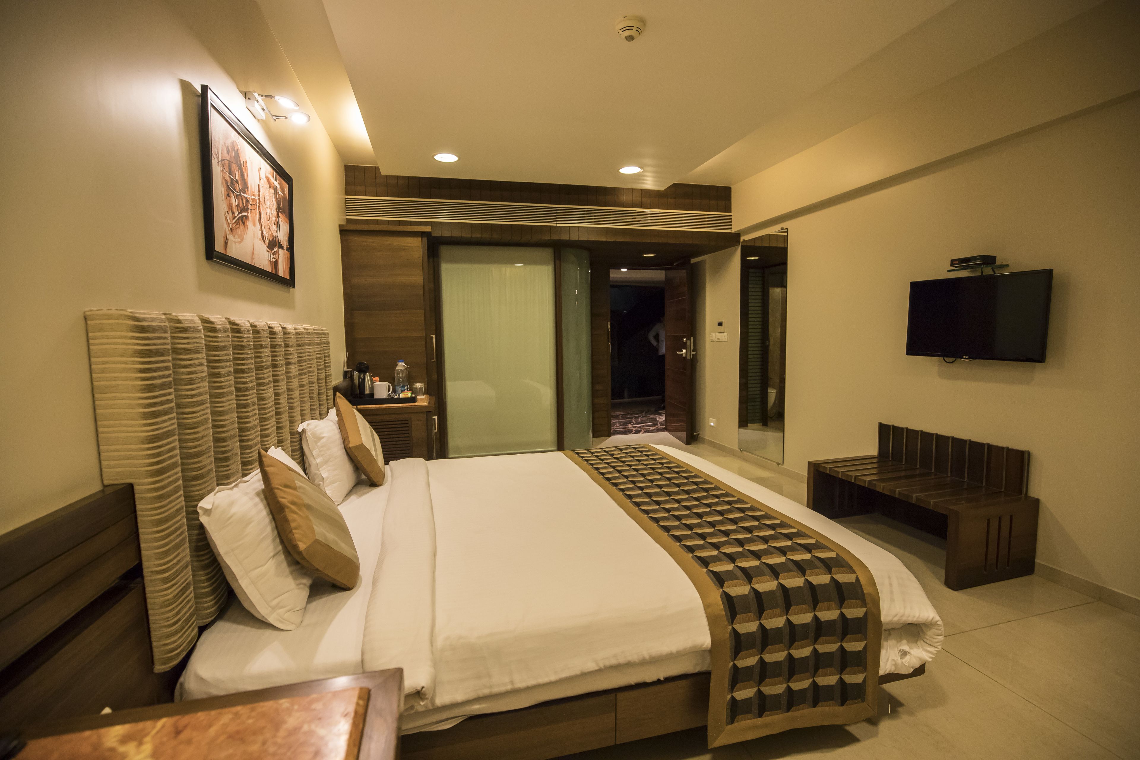 Una habitación de hotel moderna con una cama grande, un televisor de pantalla plana, una mesita de noche y un baño visible a través de una puerta abierta.