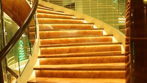 A spiral staircase with wooden steps and glass railings, leading to an upper floor. - Bizz The Hotel (Rajkot)