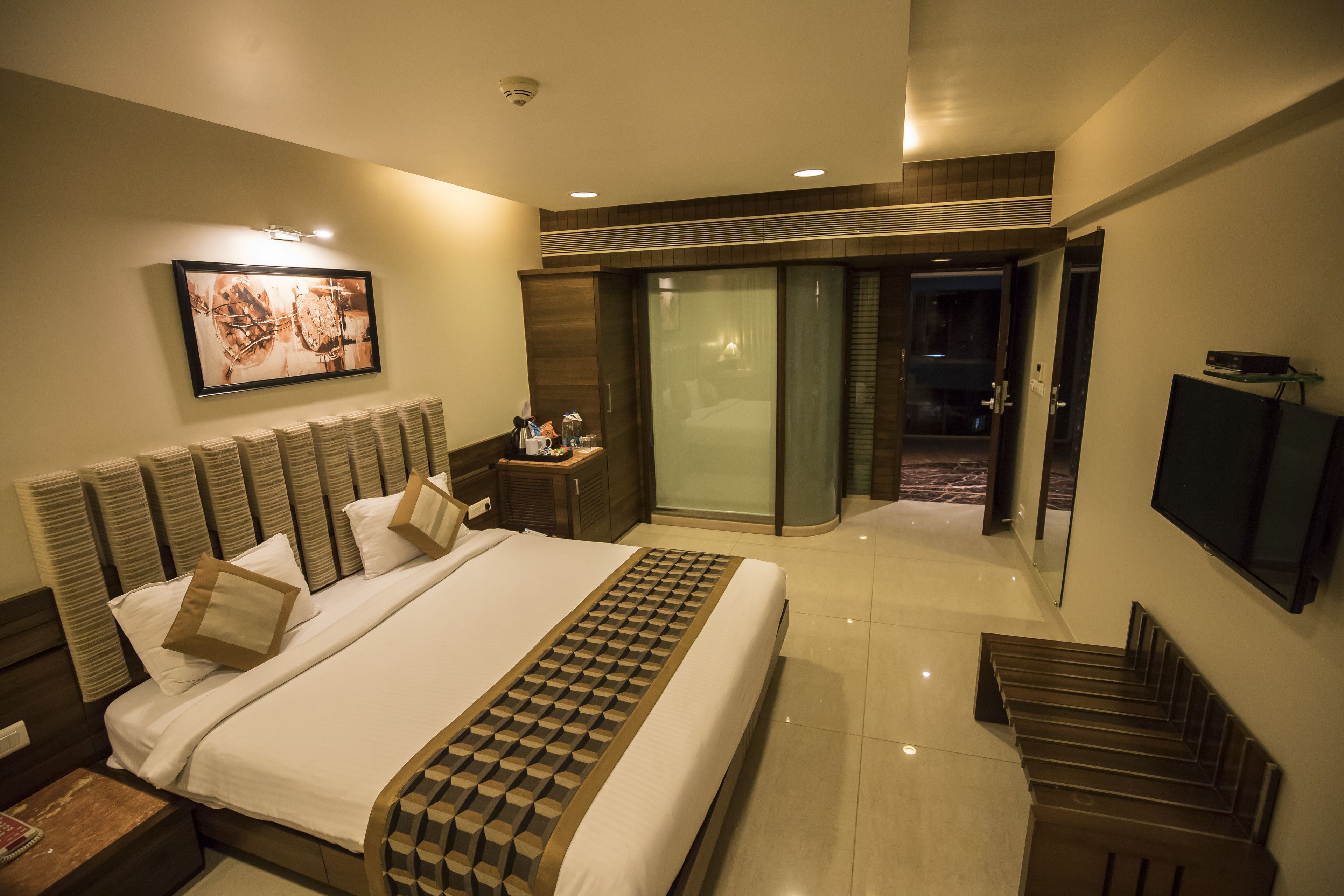 A hotel room with a large bed, a TV, a desk, and a sliding door to a balcony.