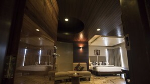 A modern hotel room with a wooden ceiling, a large bed, a sitting area with a sofa and coffee table, and a separate sleeping area with a smaller bed. - Bizz The Hotel (Rajkot)
