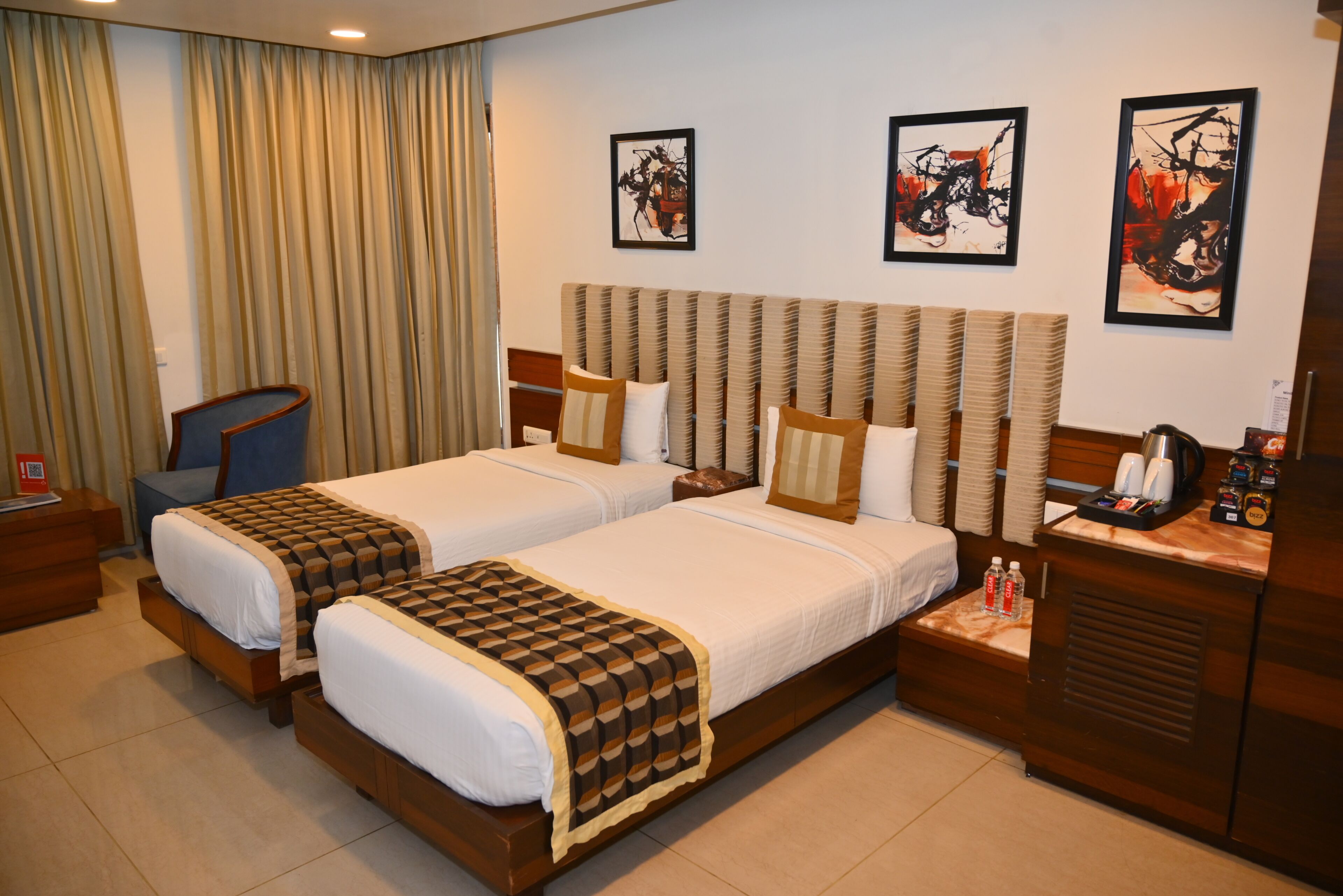 A hotel room with two beds, a desk, a chair, and artwork on the walls.