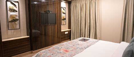 A hotel room with a large bed, wooden paneling, a flat-screen TV, and a patterned bedspread.