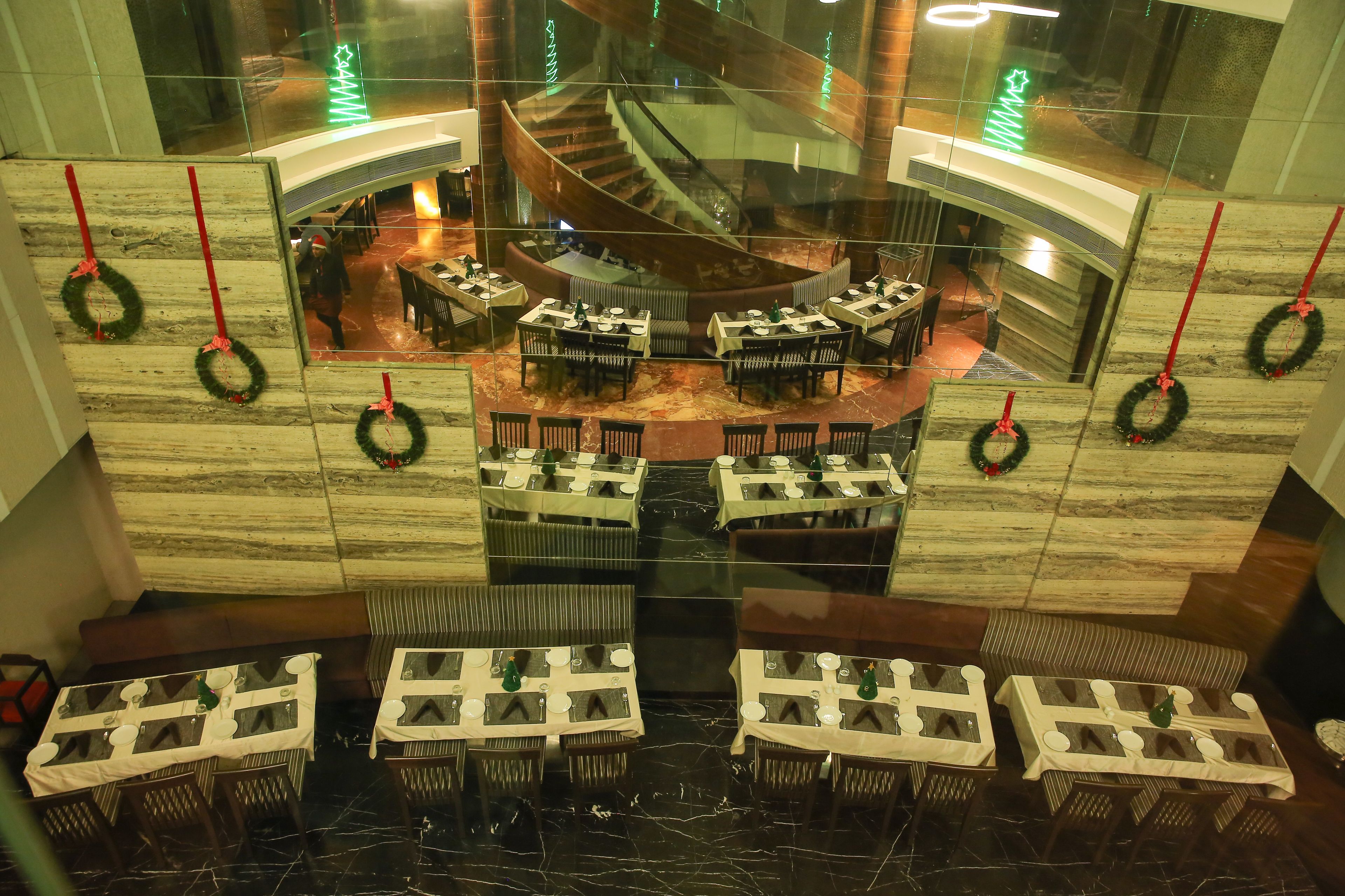 A hotel lobby with a central spiral staircase, multiple dining tables, and Christmas wreaths.