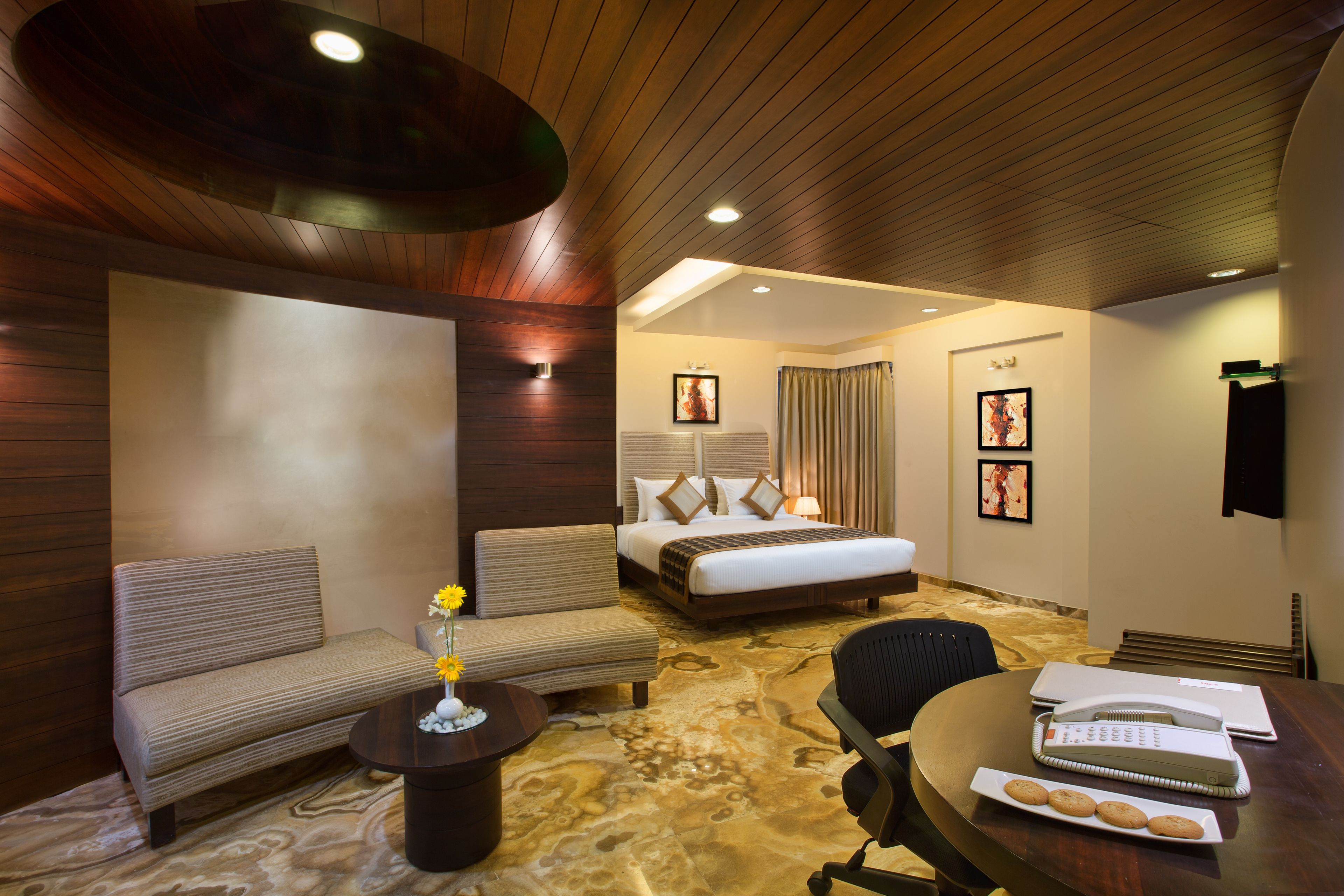 A hotel room with a bed, sofa, coffee table, and a desk with a plate of cookies.