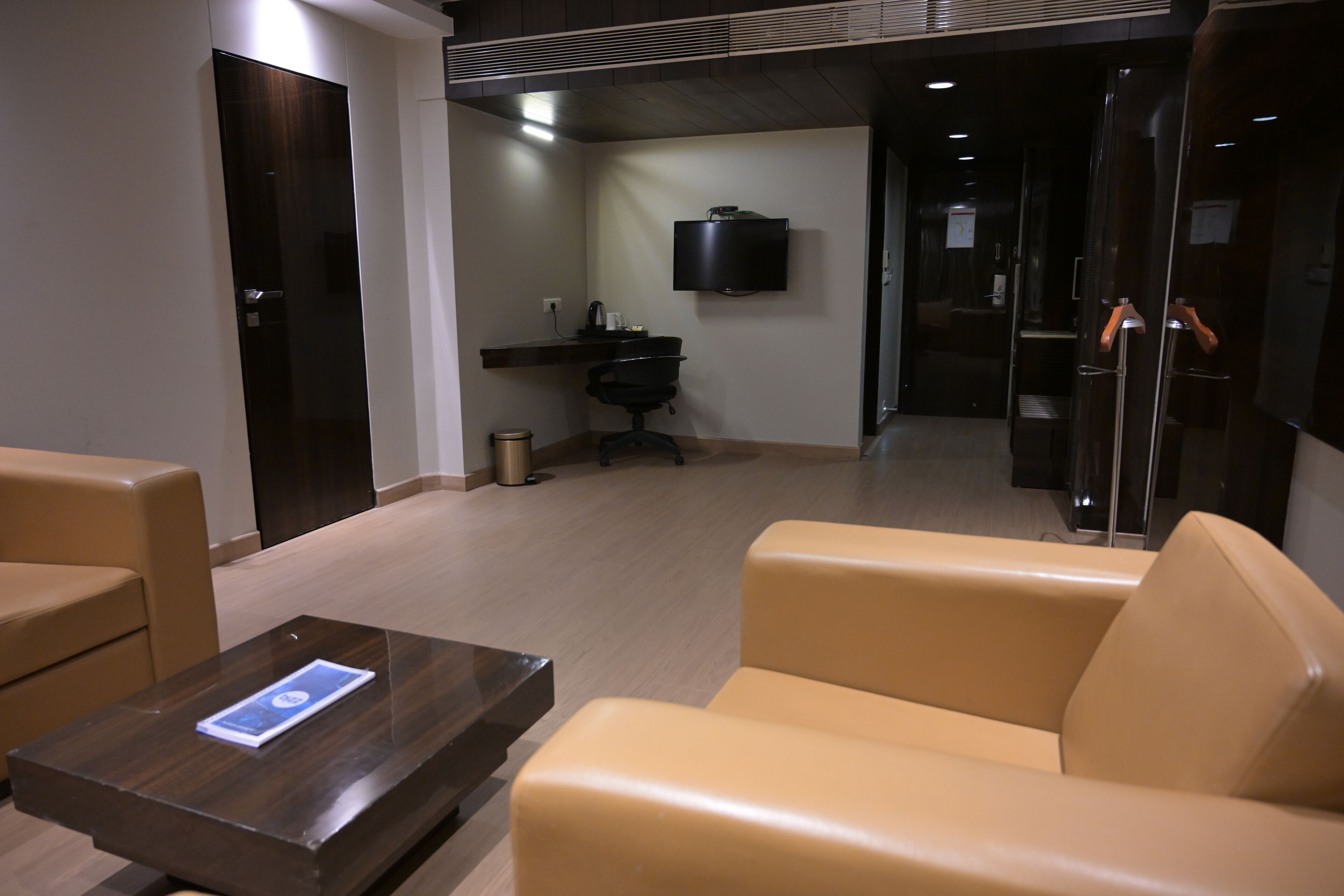 Un moderno vestíbulo de hotel con asientos de cuero, un televisor de pantalla plana en la pared y un escritorio pequeño con una cafetera.