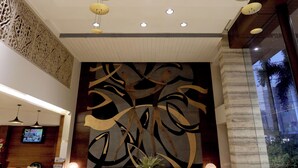 A lobby with a large abstract wall art, a reception desk, and yellow sofas arranged in a semi-circle. - Bizz The Hotel (Rajkot)