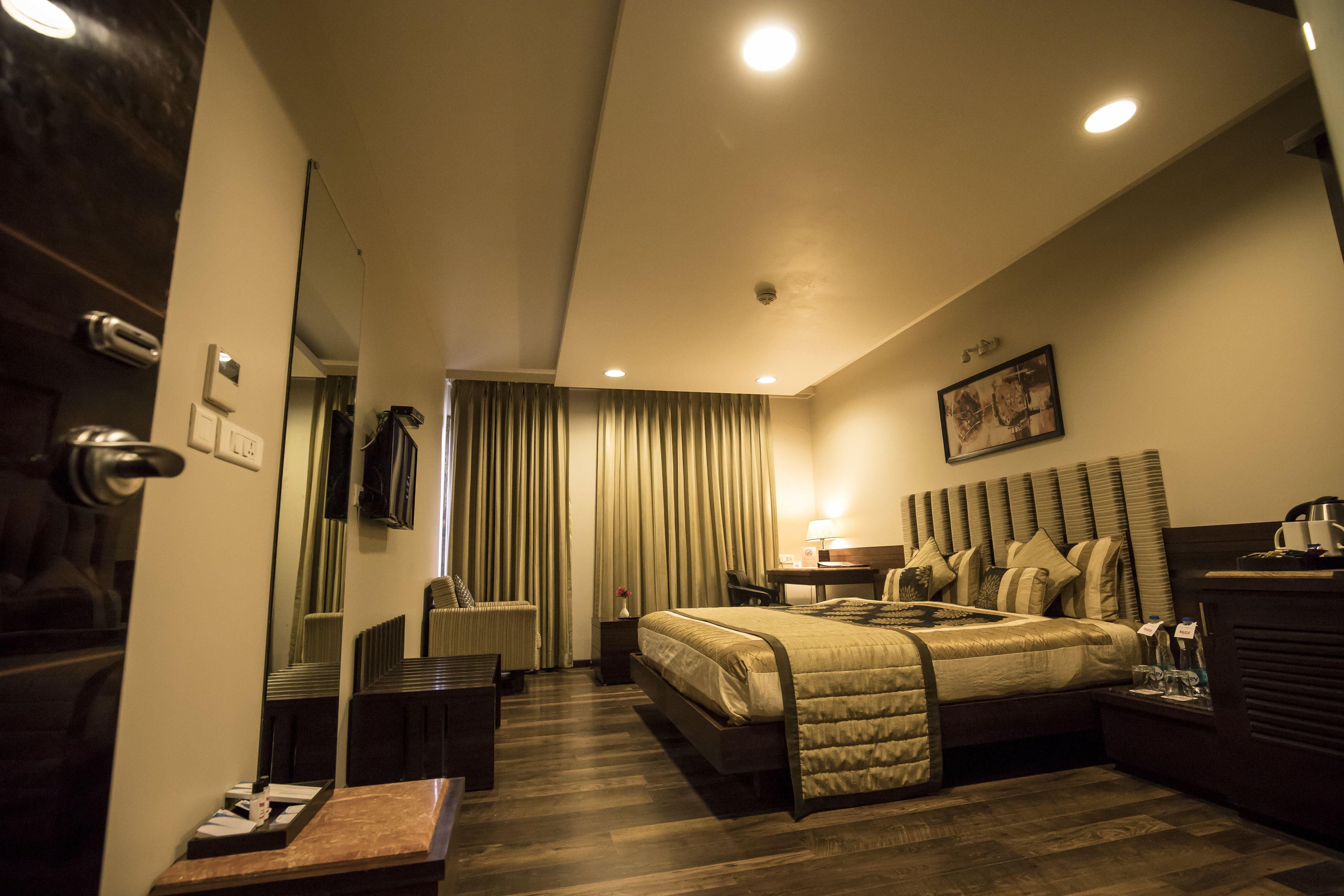 A hotel room with a bed, bedside table, lamp, and a view of the hallway.