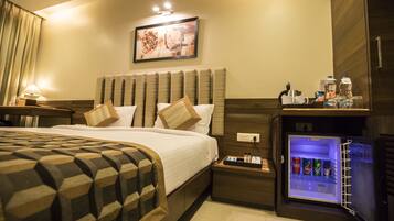 A hotel room with a bed, a nightstand, a wall-mounted refrigerator, and a painting on the wall.