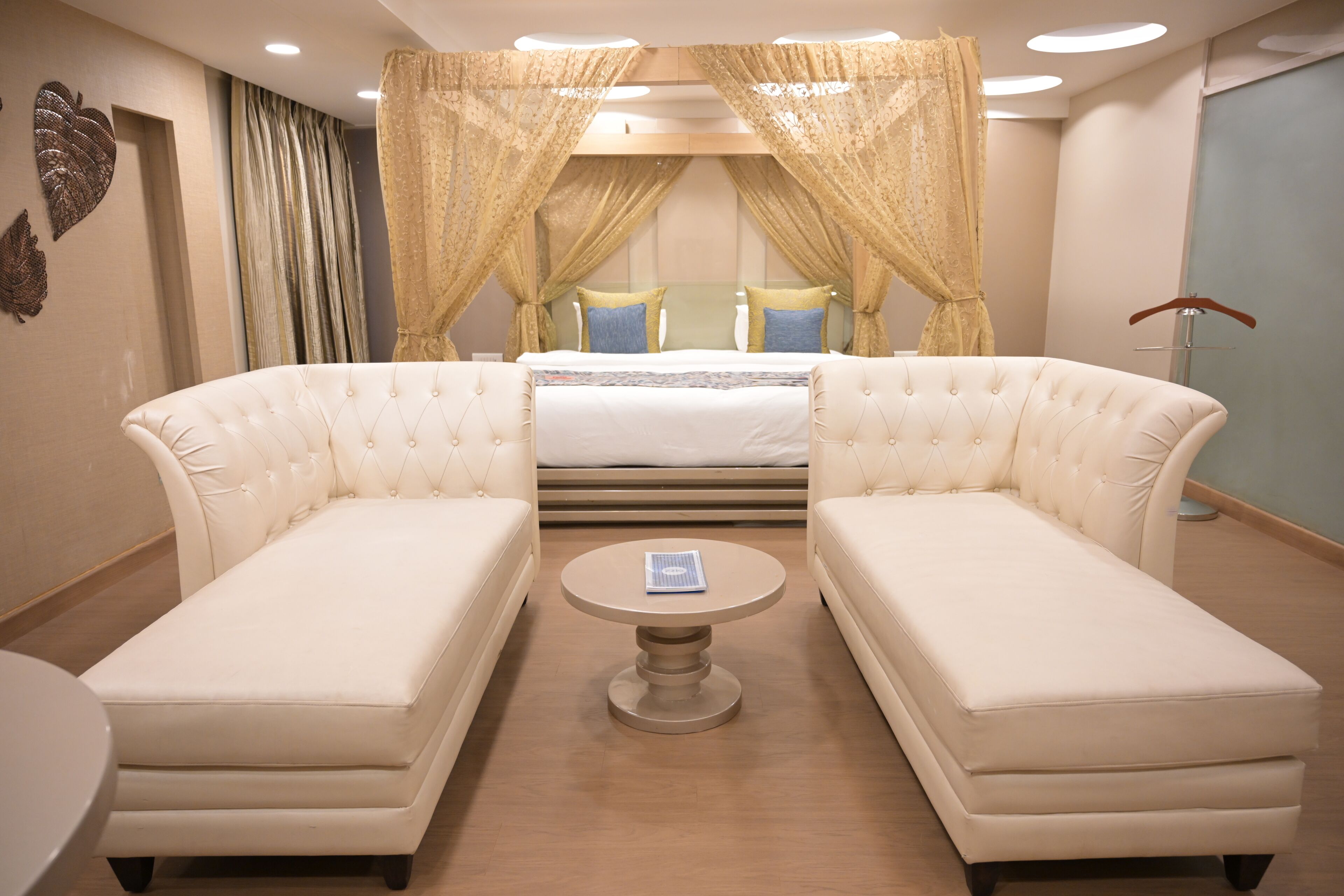 A hotel room with a large bed, two white sofas, a small round table, and a canopy bed with curtains.