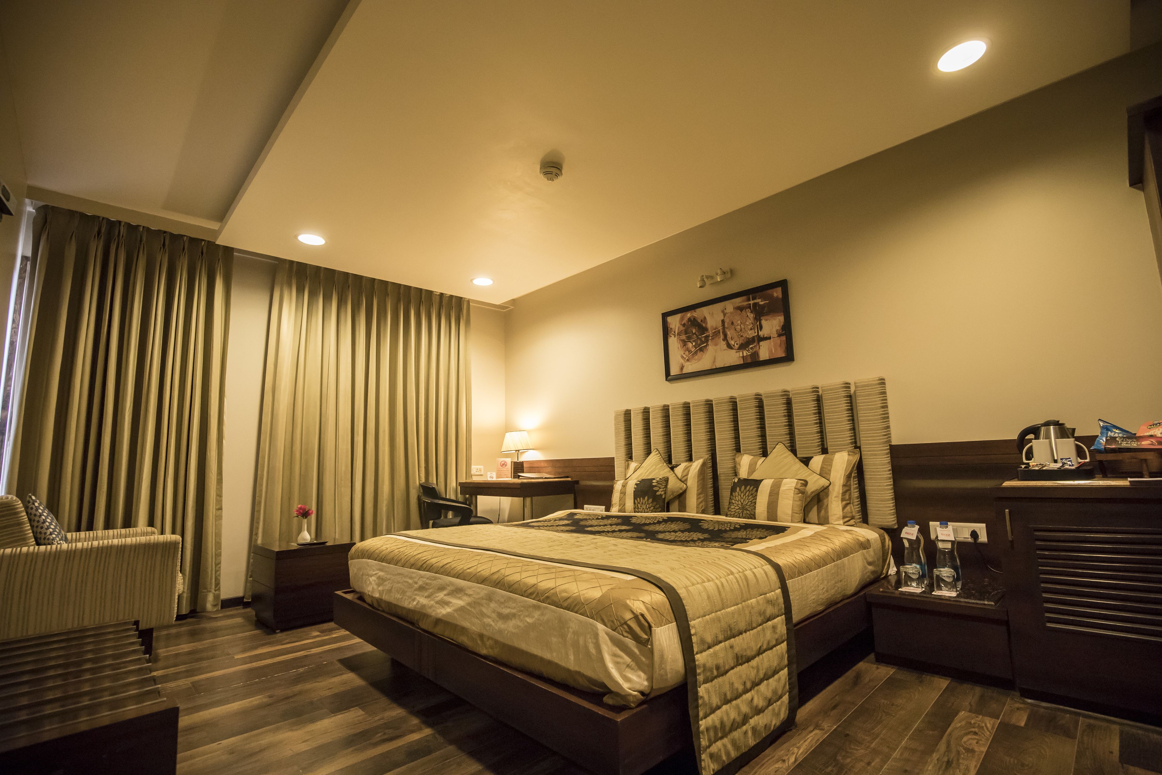 A hotel room with a large bed, a desk, a chair, a nightstand, and a painting on the wall.
