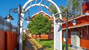 A pathway leading to a building with a red roof and white walls, flanked by black lampposts and a white archway.