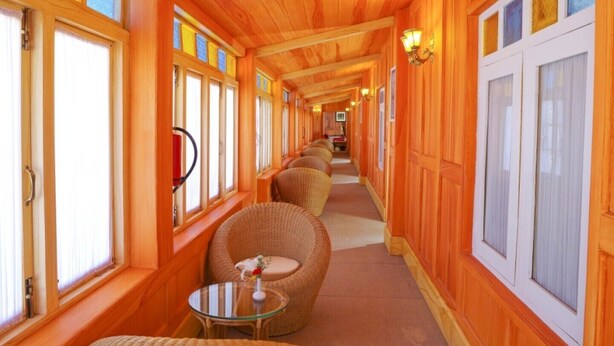A corridor with wooden walls and large windows, wicker chairs, and a small table with a vase.