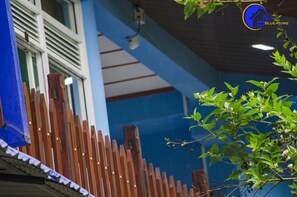 A wooden fence with a blue wall and a window with white shutters in the background. - New Blue Home (Ella)
