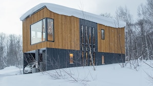 A modern wooden cabin with large windows and a car parked outside. - Ikigai (Kutchan)